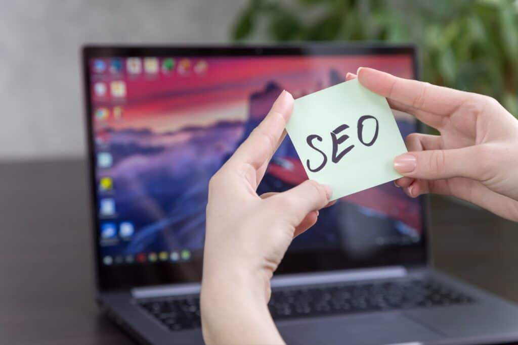 SEO concept with SEO on a post it note in the foreground with a computer in the background