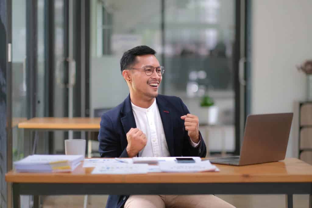 Asian male business owner standing with a computer showing happiness because his buyer intent keywords are getting conversions