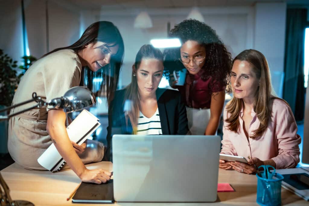 Four businesswomen at a workspace in front of a laptop talking about the latest google review left for the business they work for.